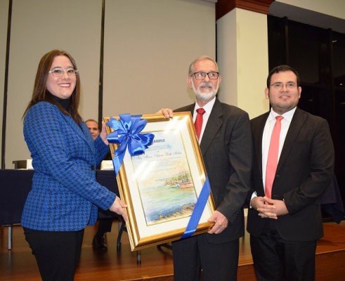 Recibiendo el pergamino de manos de Anna Panting, en presencia de Lester Herrera de la Agencia Comunica.