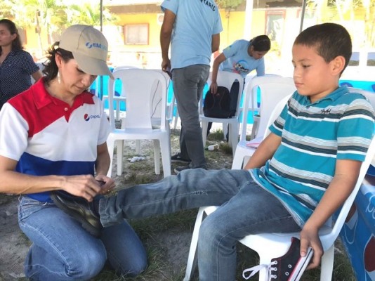 Laura Elvir, Coordinadora de Responsabilidad Social de Emsula personalmente atiendo a los niños poniéndoles el calzado nuevo para que asistan a clases